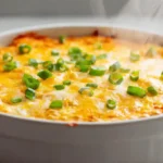 Keto buffalo chicken dip in a white baking dish with melted cheese and green onions