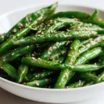 Miso green beans in a modern white bowl, shot from a 45-degree angle with sesame glaze and sesame seeds.